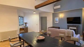 A spacious living area with a long dining table, comfortable seating, a fireplace, and a television mounted on the wall.