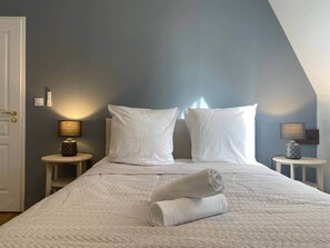 A neatly made bed with white linens and pillows, two bedside tables with lamps, and a door to the left. - «Cathédrale» 5* castle-facing Suite, 7 guests (Blois)