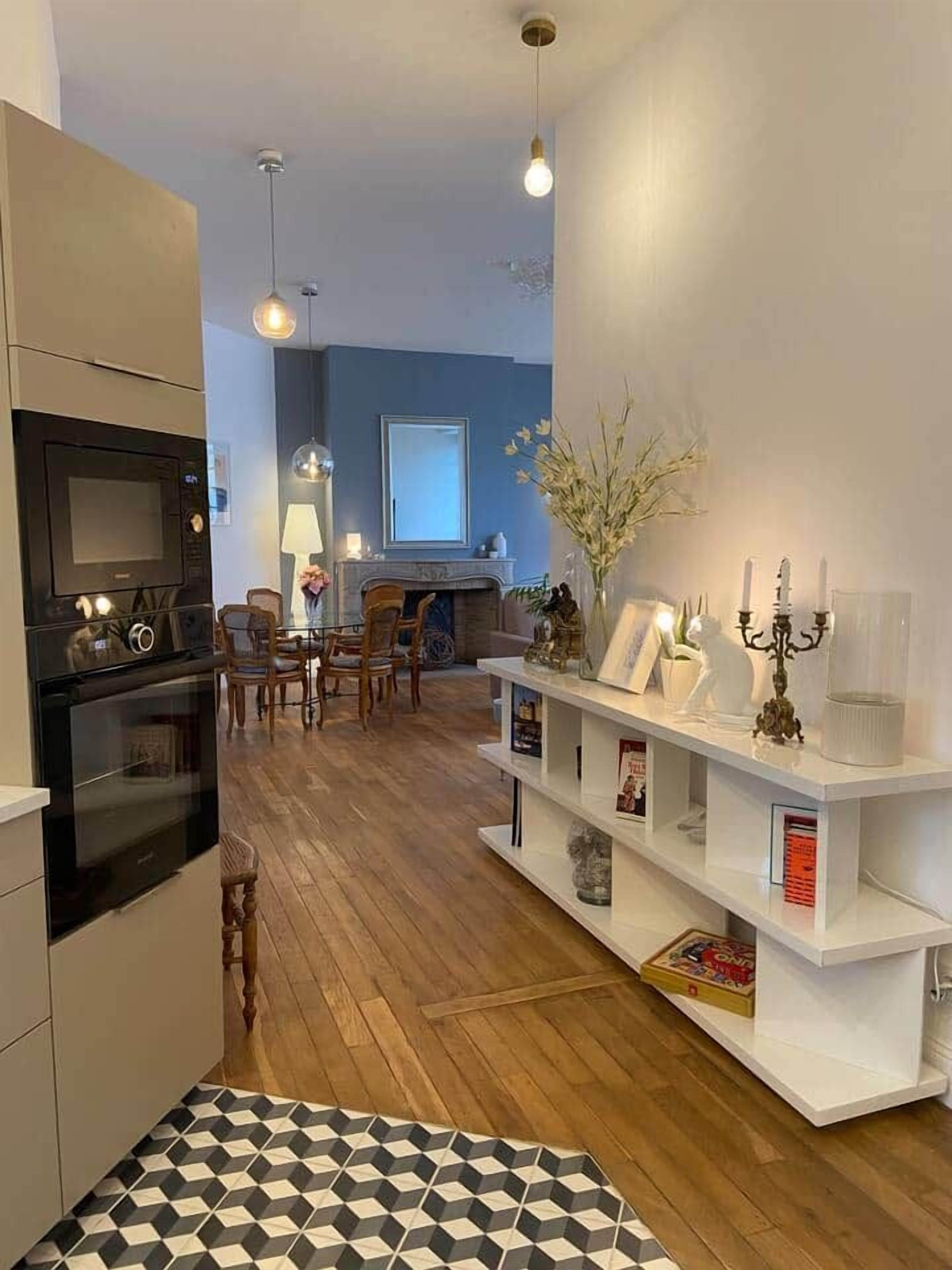 A modern kitchen with built-in appliances, a dining area with wooden chairs, and a white console table with decorative items.