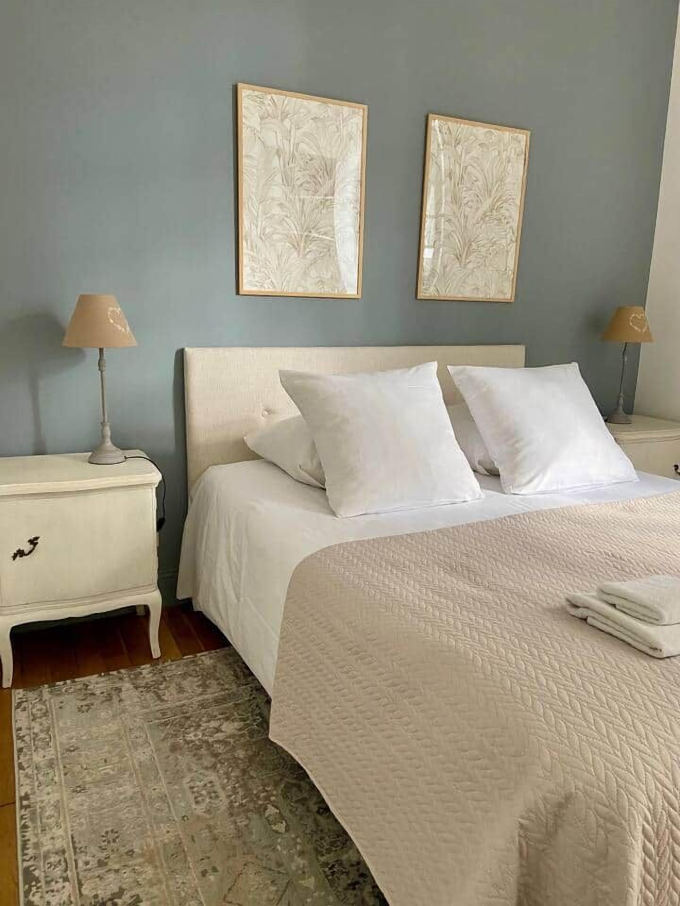 A bedroom with a bed, two nightstands, a lamp on each, and two wall-mounted artworks.