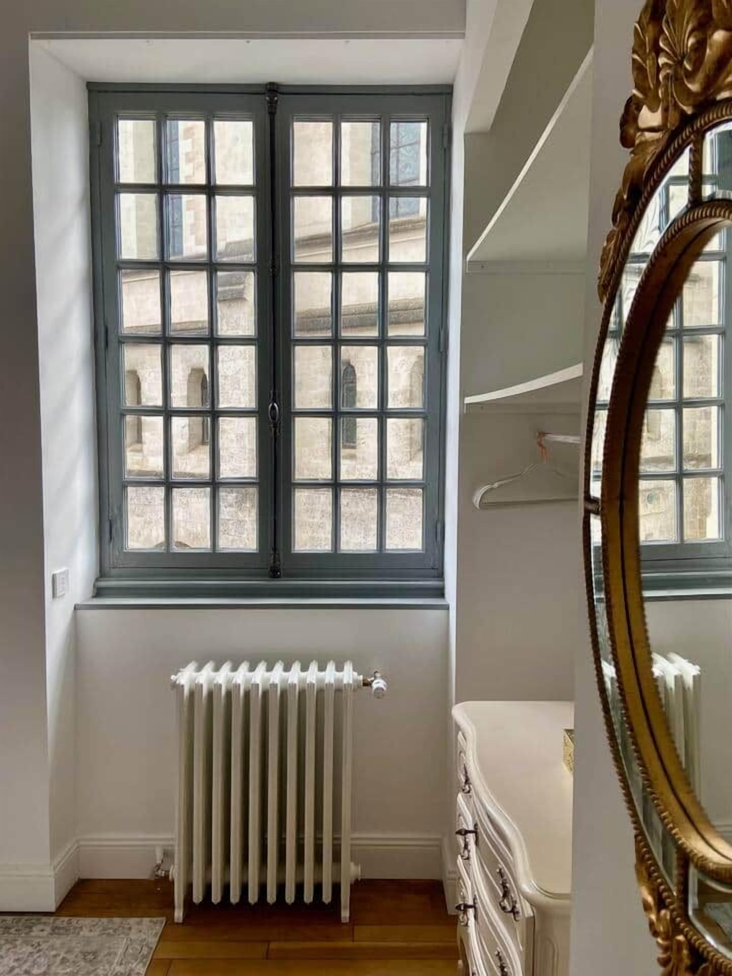 A room with a large window, a radiator, a dresser, and a mirror.