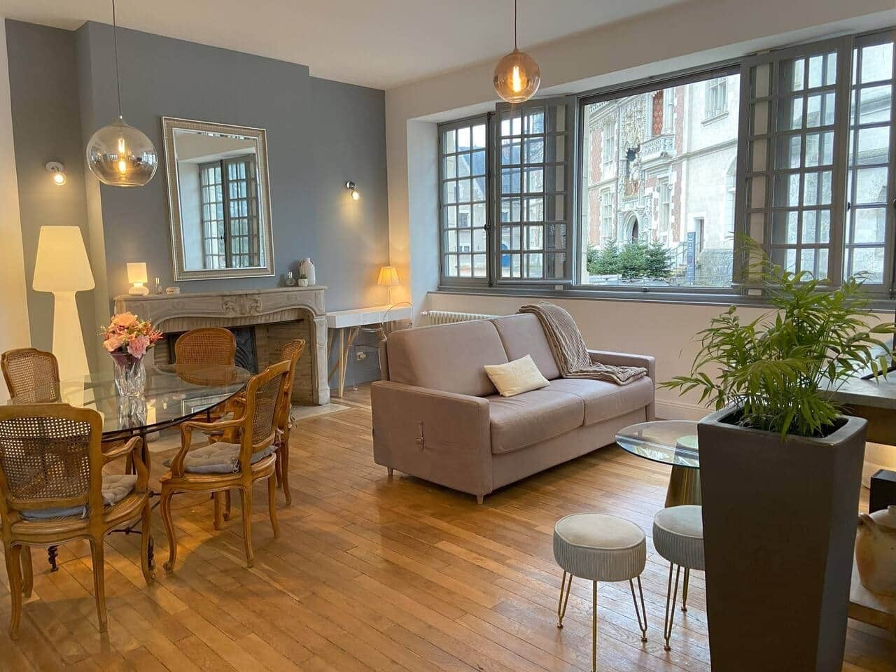 Una sala de estar moderna con una mesa de comedor de vidrio, un sofá y un amplio ventanal con vistas a edificios.