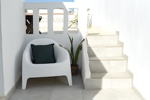 A white chair with a dark cushion, a potted plant, and a set of stairs against a white wall.