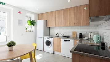 A modern kitchen with wooden cabinets, a built-in washing machine, a coffee maker, and a kettle on the countertop.