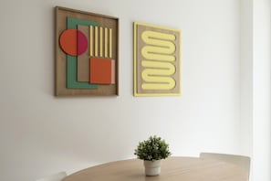 Two abstract art pieces on a wall, a potted plant on a round table.