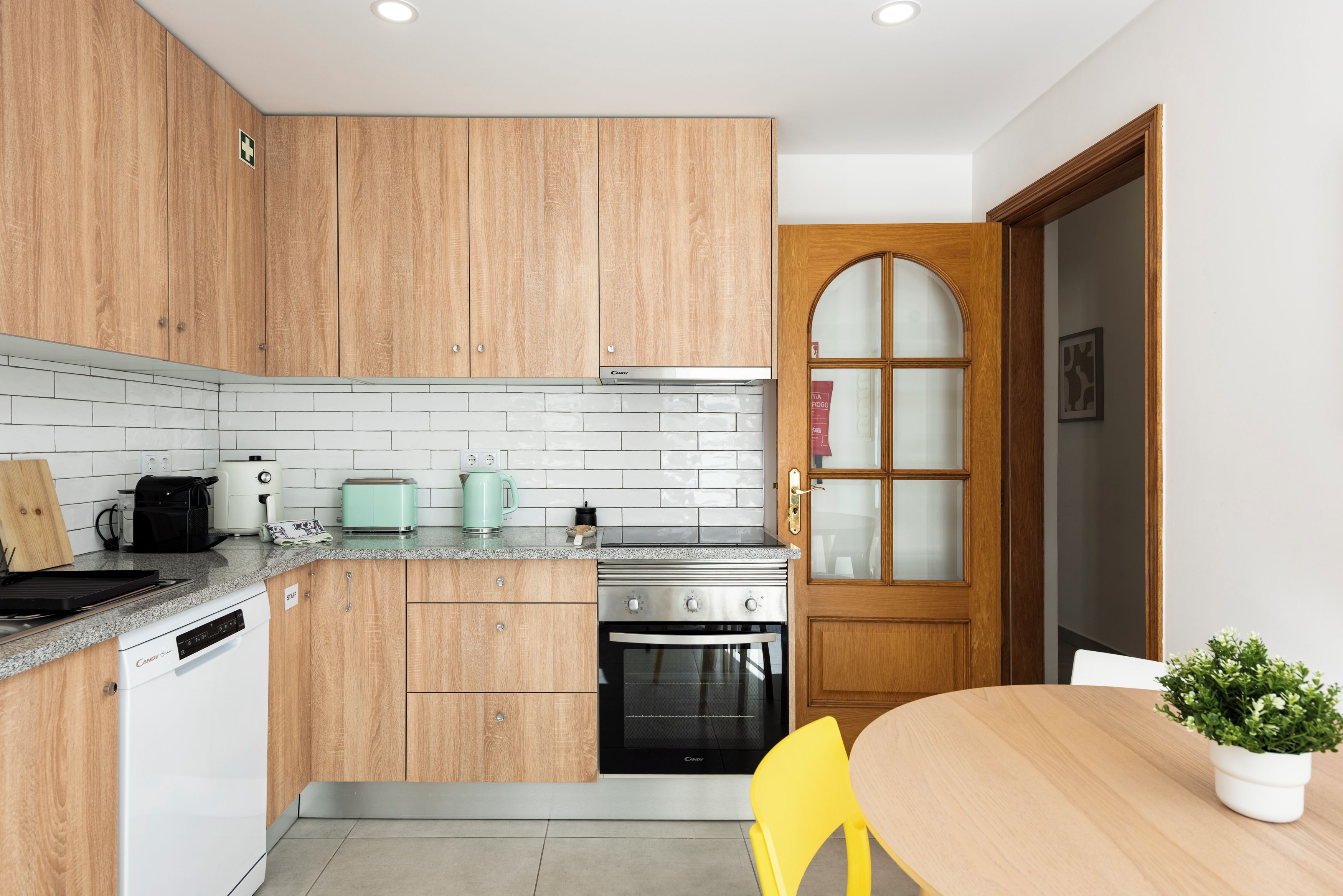 Une cuisine avec des meubles en bois, un crédence carrelée de couleur blanche, une cuisinière, un grille-pain et une machine à café.