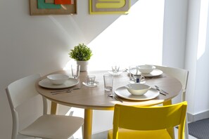Een eettafel met witte borden, kommen en bestek, een kleine potplant en een gele stoel.