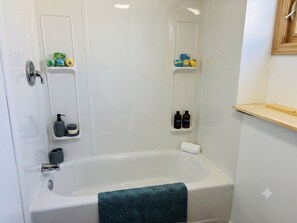 A bathroom with a bathtub, shelves with toiletries, and a towel rack. - Parkwood Nest | 2BR Home Base for Cape Breton (Sydney)