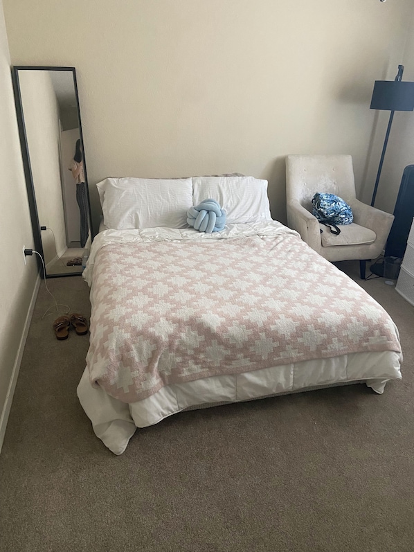 A bedroom with a bed, a chair, a mirror, and a pair of shoes.