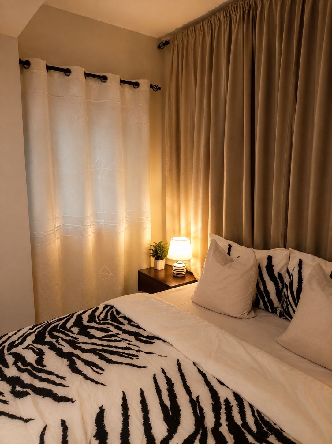 Una camera d'albergo con un letto, un comodino con una lampada e delle tende.