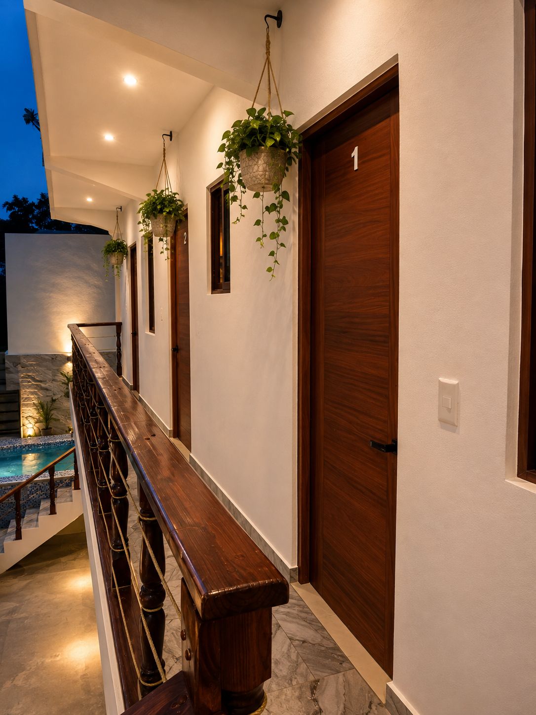 Exterior d'un edifici modern amb una banca de fusta, plantes penjants i una zona de piscina.
