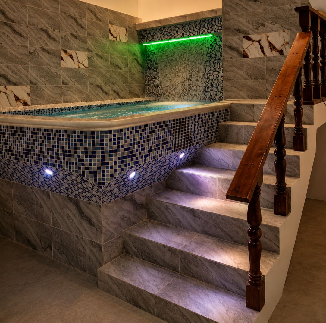 Área de spa com hidromassagem em mosaico adjacente a uma escadaria de mármore.