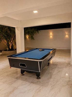 A pool table in a room with a tiled floor and a wall-mounted light fixture.