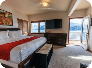 A bedroom with a bed, a dresser, a TV, and a balcony with a mountain view. -  Waterfront Home in Bayview with private boat dock on Lake Pend Oreille (Bayview)