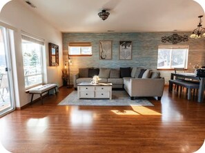 A spacious living room with a sofa, a coffee table, and a dining area with a bench. -  Waterfront Home in Bayview with private boat dock on Lake Pend Oreille (Bayview)