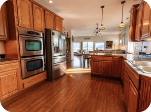 A kitchen with wooden cabinets, stainless steel appliances, and a dining area with a view. -  Waterfront Home in Bayview with private boat dock on Lake Pend Oreille (Bayview)