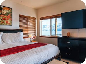 A bedroom with a bed, a nightstand, a dresser, and a window with a view of mountains. -  Waterfront Home in Bayview with private boat dock on Lake Pend Oreille (Bayview)