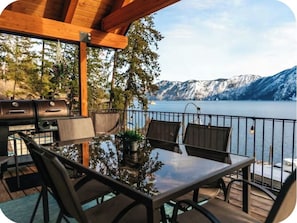 An outdoor dining area with a view of a lake and mountains, featuring a grill and seating. -  Waterfront Home in Bayview with private boat dock on Lake Pend Oreille (Bayview)