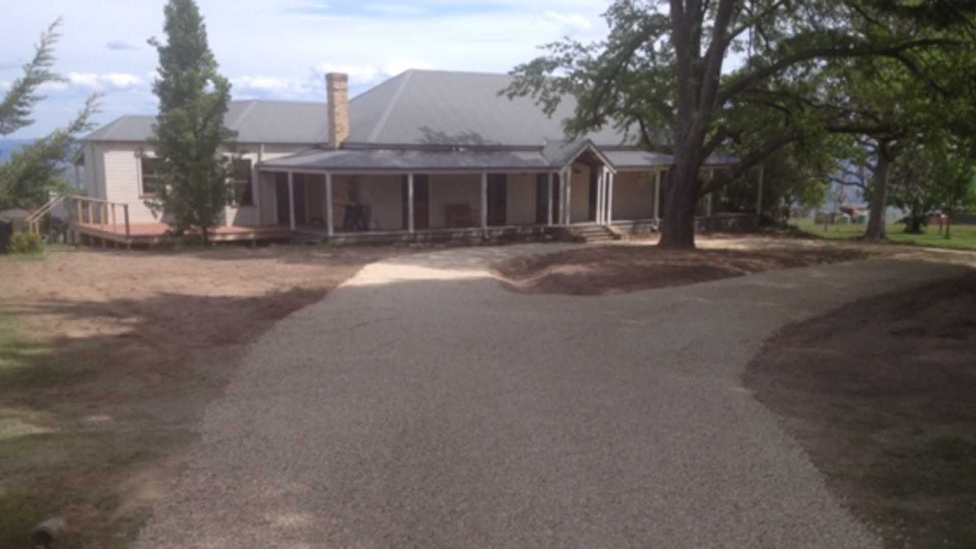 A house with a covered porch, a driveway, and a large tree in the foreground.
