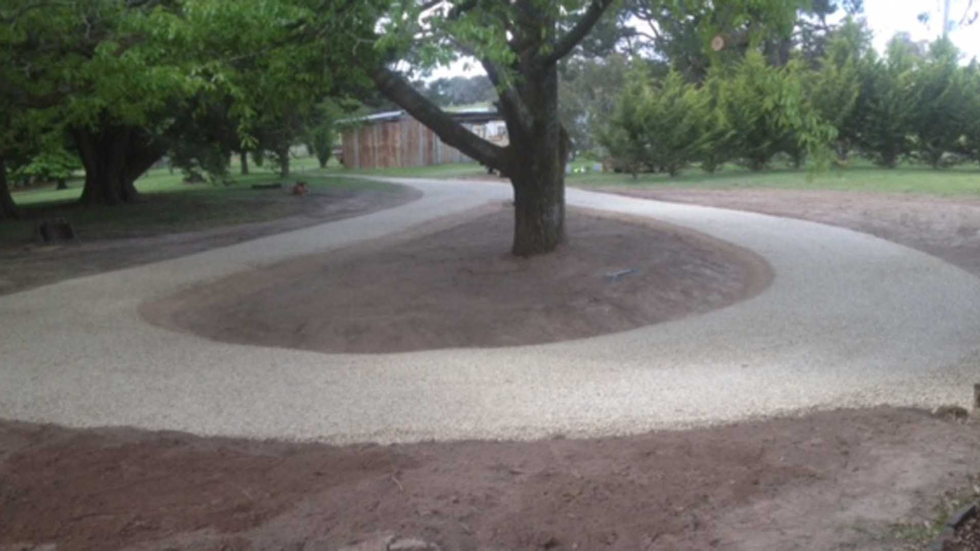 Un espace aménagé avec un arbre au centre, entouré d’un chemin circulaire en gravier.