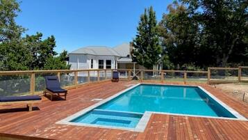 Une terrasse en bois avec une piscine, des chaises longues et une maison en arrière-plan.
