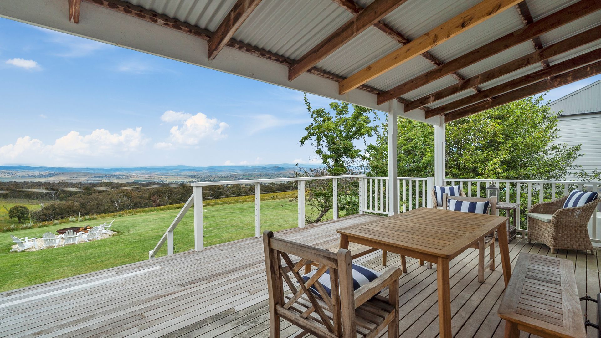 A wooden deck with a table and chairs, overlooking a grassy landscape with distant hills.