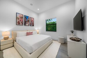 Un dormitorio moderno con una cama grande, mesitas de noche, un televisor de pantalla plana y un ventanal con vistas a zonas verdes.