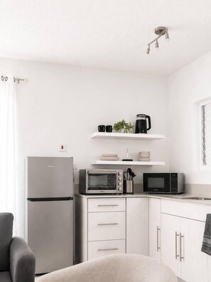 A compact kitchen with a refrigerator, microwave, and oven. There are white cabinets and a small countertop. - Modern Refurbed Condo | Resort Pool | Sleeps 4 (Ocho Rios)