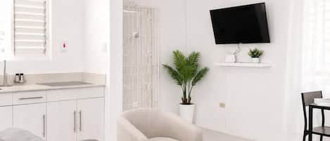 A modern living room with a grey sofa, a small round coffee table, a beige armchair, a flat-screen TV mounted on the wall, and a ceiling fan.
