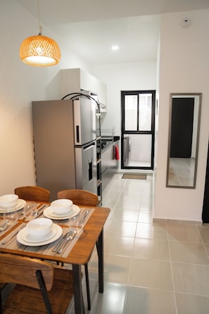 Une cuisine moderne équipée d’appareils électroménagers en acier inoxydable, un coin repas avec une table en bois pour quatre personnes, et une vue sur le salon grâce à une porte ouverte.