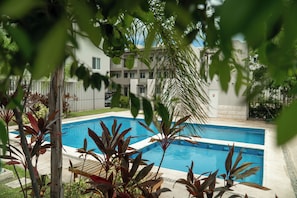 Ein Pool, umgeben von Pflanzen und einem Gebäude mit vielen Fenstern.