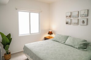 Ein Schlafzimmer mit einem Bett, einem Nachttisch mit Lampe, einem Fenster und Wandbildern.