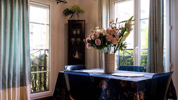 Un coin repas avec une table dressée pour deux personnes, un vase de fleurs et un buffet contenant de la verrerie.