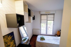 Ein Schlafzimmer mit einem Bett, einem Heizkörper, einem Fenster mit Jalousien und eingebauten Regalen.
