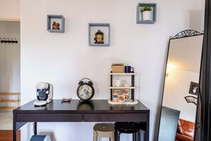 Ein Schreibtisch mit einer Kaffeemaschine, einem Wecker und einem Regal mit Tassen und einem Korb.