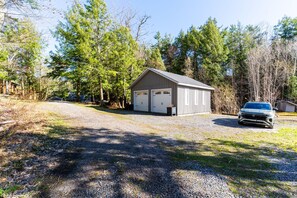 Un garage pour deux voitures, avec une allée en gravier, entouré d’arbres et avec une voiture garée devant.