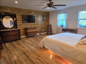 A bedroom with a wooden floor, a bed, a dresser, a chair, a television mounted on the wall, and a ceiling fan. - Spacious 4BR house tranquil lakeview w boat launch beach access/park extra prkng (Jacksonville)