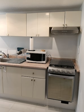 A kitchen with white cabinets, a microwave, a gas stove, and a sink. - Beautiful New Apartment in Downtown Coyoacán (Ciudad de México)