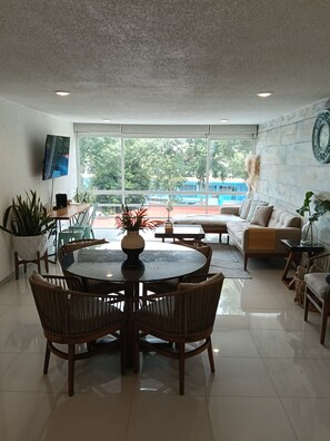 A modern living room with a round dining table, comfortable seating, a flat-screen TV, and a view of a swimming pool. - Beautiful New Apartment in Downtown Coyoacán (Ciudad de México)