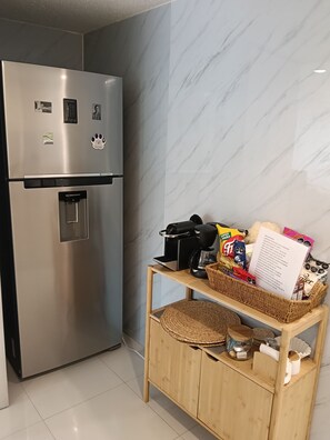 A kitchen with a stainless steel refrigerator, a wooden cabinet with a woven basket, and a coffee maker on a shelf. - Beautiful New Apartment in Downtown Coyoacán (Ciudad de México)