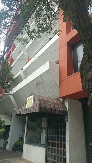 A multi-story building with a red and grey facade, a small awning with a sign, and a barred window. - Beautiful New Apartment in Downtown Coyoacán (Ciudad de México)