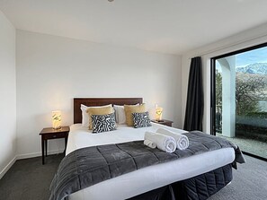 Ein Hotelzimmer mit einem großen Bett, einem Nachttisch, einer Lampe und Blick ins Freie.