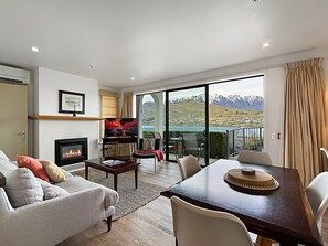 Ein modernes Wohnzimmer mit Kamin, Essbereich und einer großen Schiebeglastür, die auf einen Balkon mit Bergblick führt.