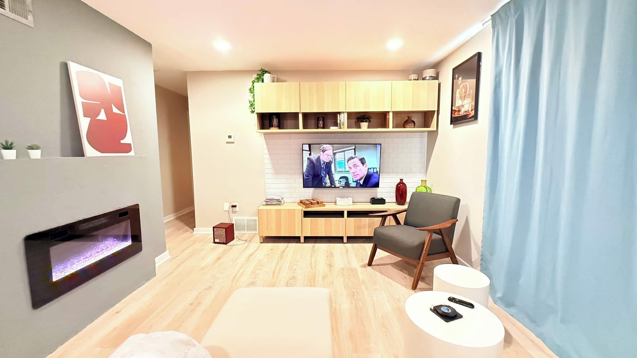 A modern living room with a flat-screen TV, a fireplace, a dining area, and a seating area with a chair and a small table.