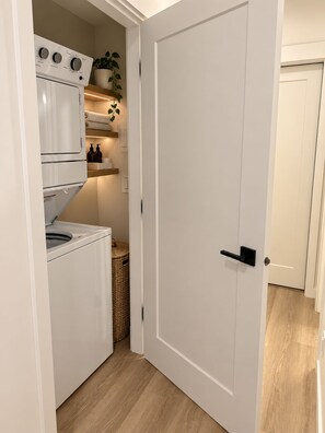 Een kleine wasruimte met een wasmachine, droger en planken met toiletartikelen.