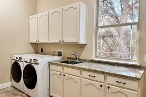 A laundry room with a washing machine, a sink, and cabinets.