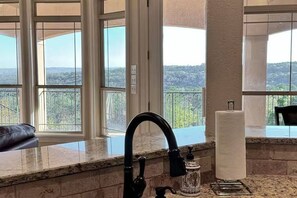 A kitchen with a large window, a black faucet, and a paper towel holder.