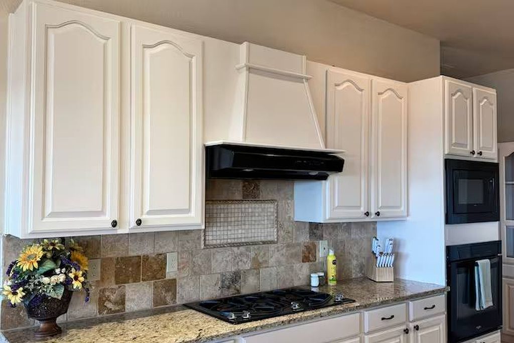 A kitchen with white cabinetry, a granite countertop, a black stove, and a backsplash with a grid pattern.