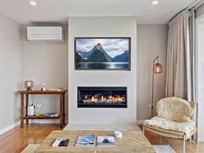 A living room with a fireplace, a mounted TV, and a comfortable chair. - Newly Renovated Lakefront Retreat, Sleeps 2 (Queenstown)