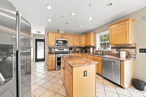 Cocina con armarios de madera, electrodomésticos de acero inoxidable y piso de baldosas.